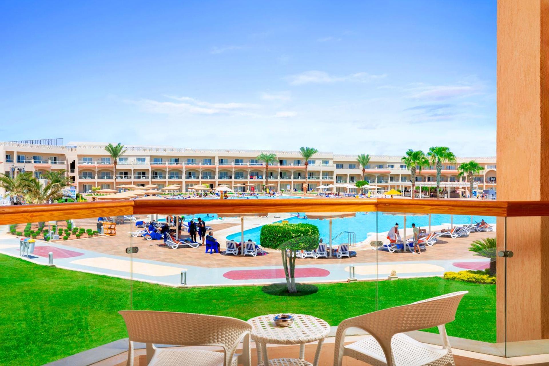 Hotel Royal Albatros Moderna - Families and couples only à Charm el-Cheikh Extérieur photo The photo shows a beautiful view from a balcony overlooking a pool area at a resort. In the foreground, there are two white chairs and a small table on the balcony. Below, the pool is surrounded by sun loungers and umbrellas, and there are several pe