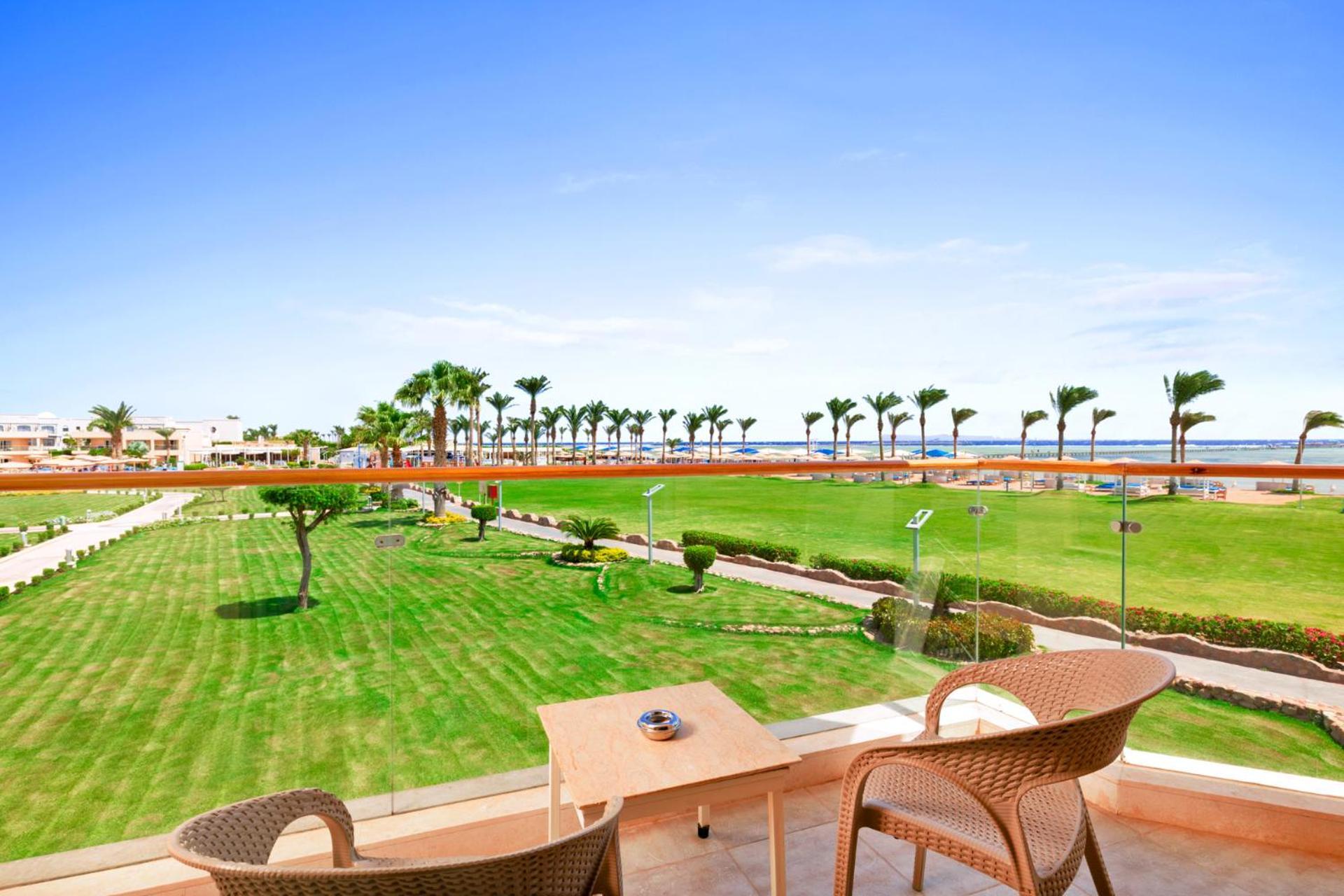 Hotel Royal Albatros Moderna - Families and couples only à Charm el-Cheikh Extérieur photo The photo shows a scenic view from a balcony overlooking a lush green lawn. There are two outdoor chairs and a small table on the balcony. In the background, palm trees line the pathway leading to the beach, which is visible in the distance under a c