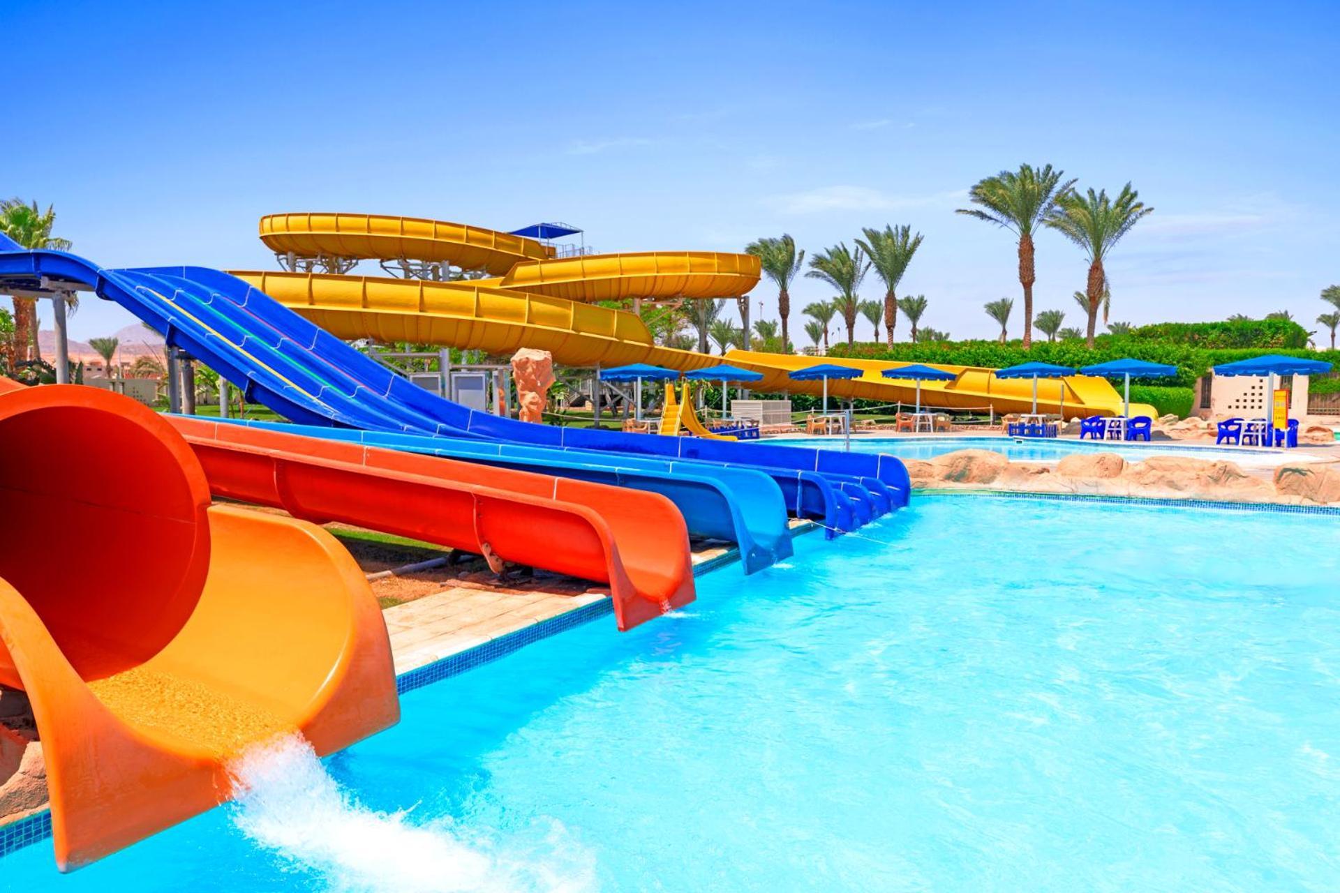 Hotel Royal Albatros Moderna - Families and couples only à Charm el-Cheikh Extérieur photo The photo shows a vibrant water park scene featuring multiple water slides of various colors, including yellow, orange, and blue. The slides are positioned above a clear blue swimming pool where water flows out. In the background, there are palm tree