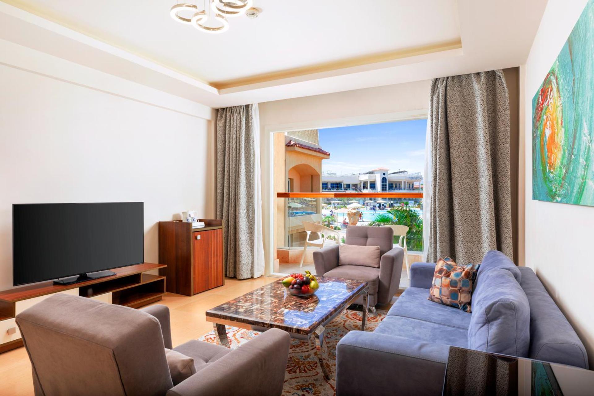 Hotel Royal Albatros Moderna - Families and couples only à Charm el-Cheikh Extérieur photo The photo shows a modern and stylish living room. It features a comfortable seating arrangement with a gray sofa and two armchairs, a coffee table in the center, and a wooden TV stand with a large flat-screen TV. There are large windows with curtains