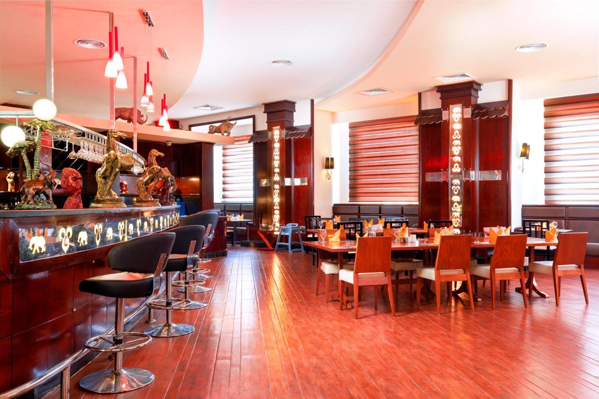Hotel Royal Albatros Moderna - Families and couples only à Charm el-Cheikh Extérieur photo The photo shows the interior of a restaurant. It features a sleek, modern design with wooden floors and a warm color palette. On the left, there is a bar area with high stools, and the bar itself is illuminated with decorative lights. The seating inc