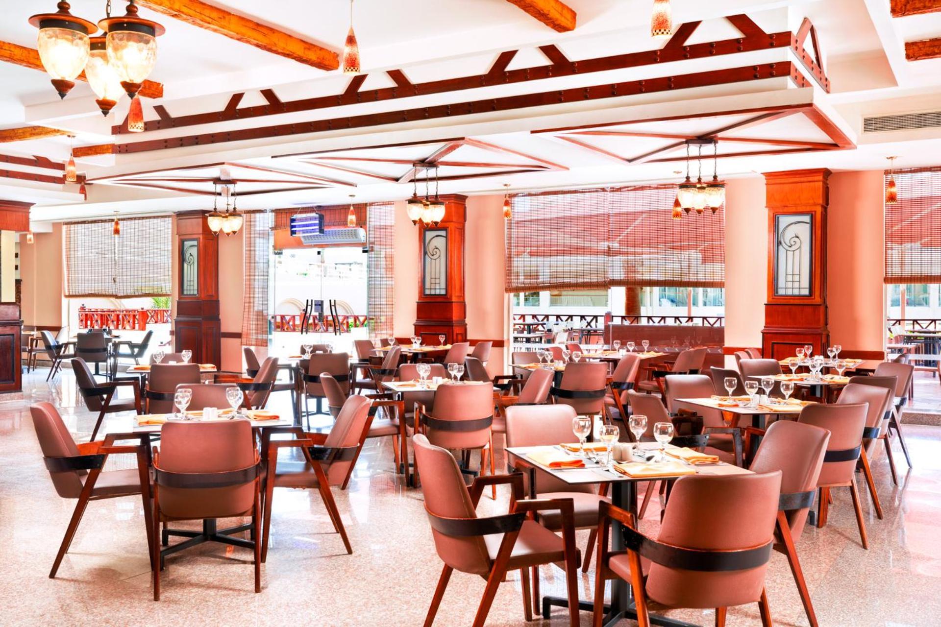 Hotel Royal Albatros Moderna - Families and couples only à Charm el-Cheikh Extérieur photo The photo shows the interior of a restaurant. It features a spacious dining area with several tables set for patrons, each equipped with cutlery and glassware. The decor includes wooden beams and pendant lighting, creating a warm and inviting atmosph