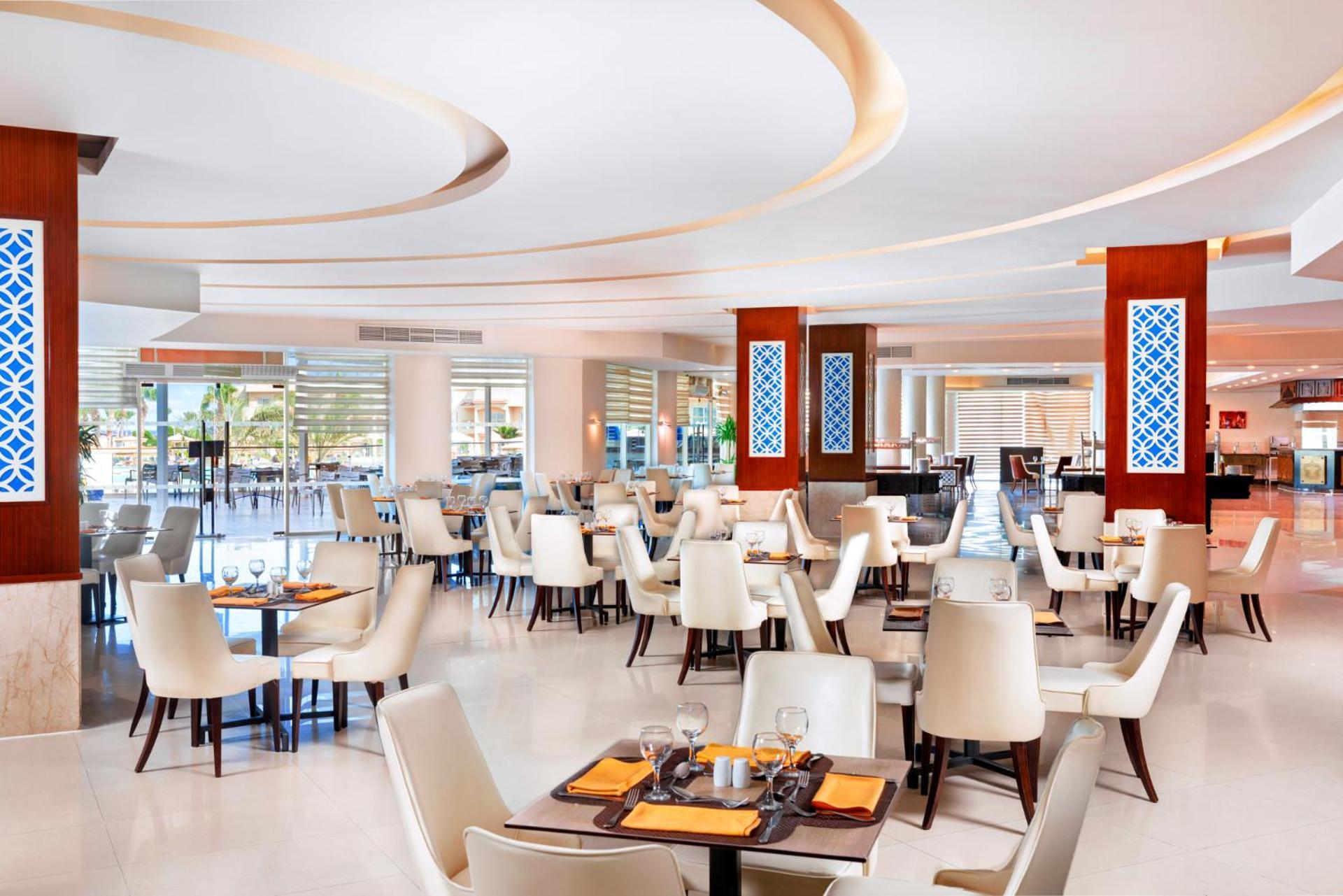 Hotel Royal Albatros Moderna - Families and couples only à Charm el-Cheikh Extérieur photo The photo shows a modern restaurant interior. The design features light, neutral colors with elegant white chairs and wooden tables. The layout includes several dining tables set for customers, creating a spacious and inviting atmosphere. There are d
