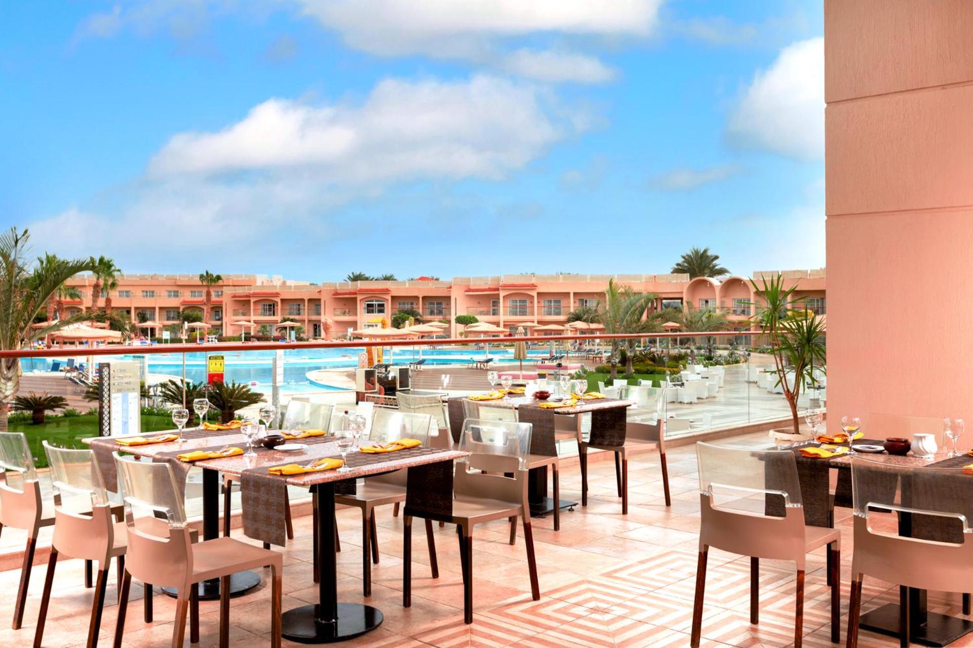 Hotel Royal Albatros Moderna - Families and couples only à Charm el-Cheikh Extérieur photo The photo shows an outdoor dining area at a resort. There are several tables set for dining, featuring elegant tableware. In the background, a large swimming pool is visible, surrounded by lush greenery and lounge chairs. The buildings beyond the poo