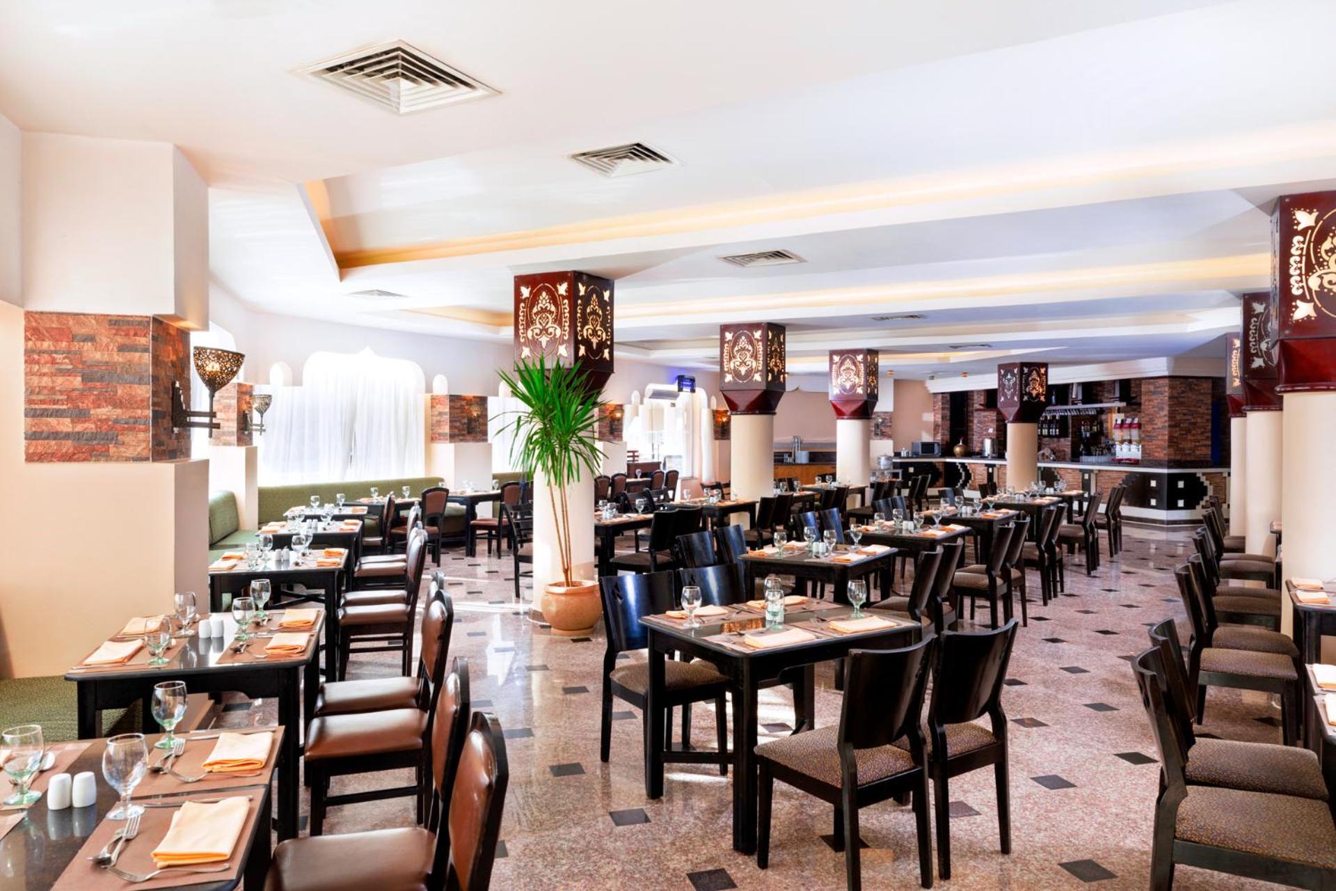 Hotel Royal Albatros Moderna - Families and couples only à Charm el-Cheikh Extérieur photo The photo shows an interior of a restaurant featuring a spacious dining area. There are several tables arranged neatly with black chairs, and each table is set with cutlery and glassware. The decor includes decorative light fixtures that have a patte