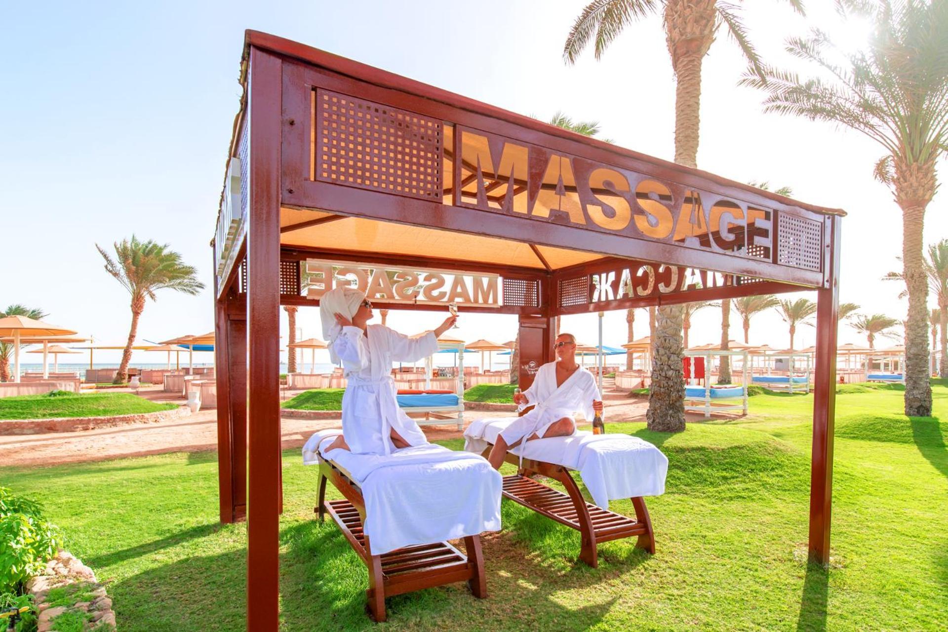 Hotel Royal Albatros Moderna - Families and couples only à Charm el-Cheikh Extérieur photo The photo shows a massage area set up in a sunny outdoor environment. There are two massage tables under a wooden canopy with the word "MASSAGE" prominently displayed. Two individuals, dressed in white robes, appear to be engaged in a massage session