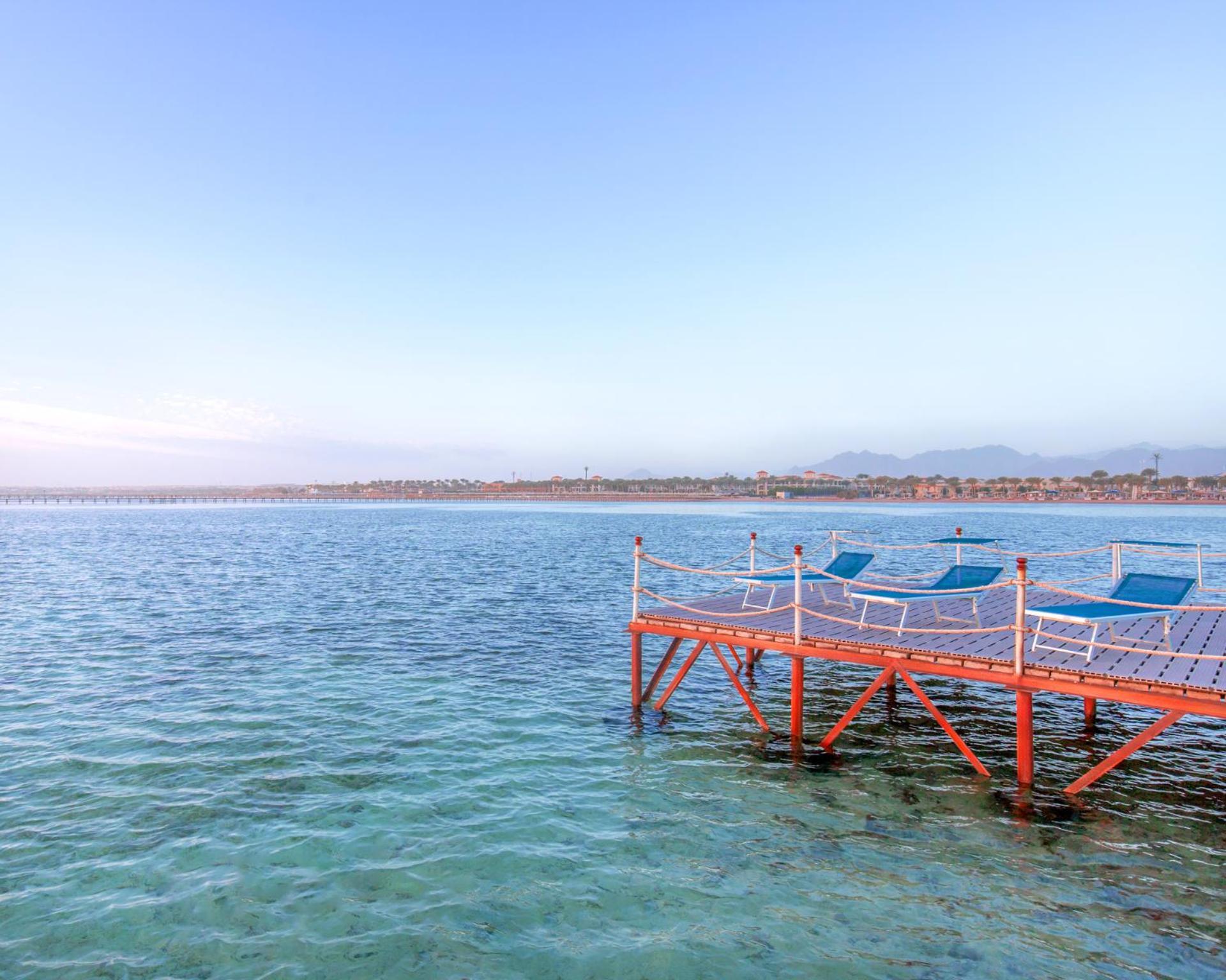 Hotel Royal Albatros Moderna - Families and couples only à Charm el-Cheikh Extérieur photo The photo shows a peaceful scene featuring a wooden dock extending into calm water. The dock is painted orange and has several blue lounge chairs placed on it, suggesting a relaxed atmosphere. In the background, there's a shoreline with some greenery