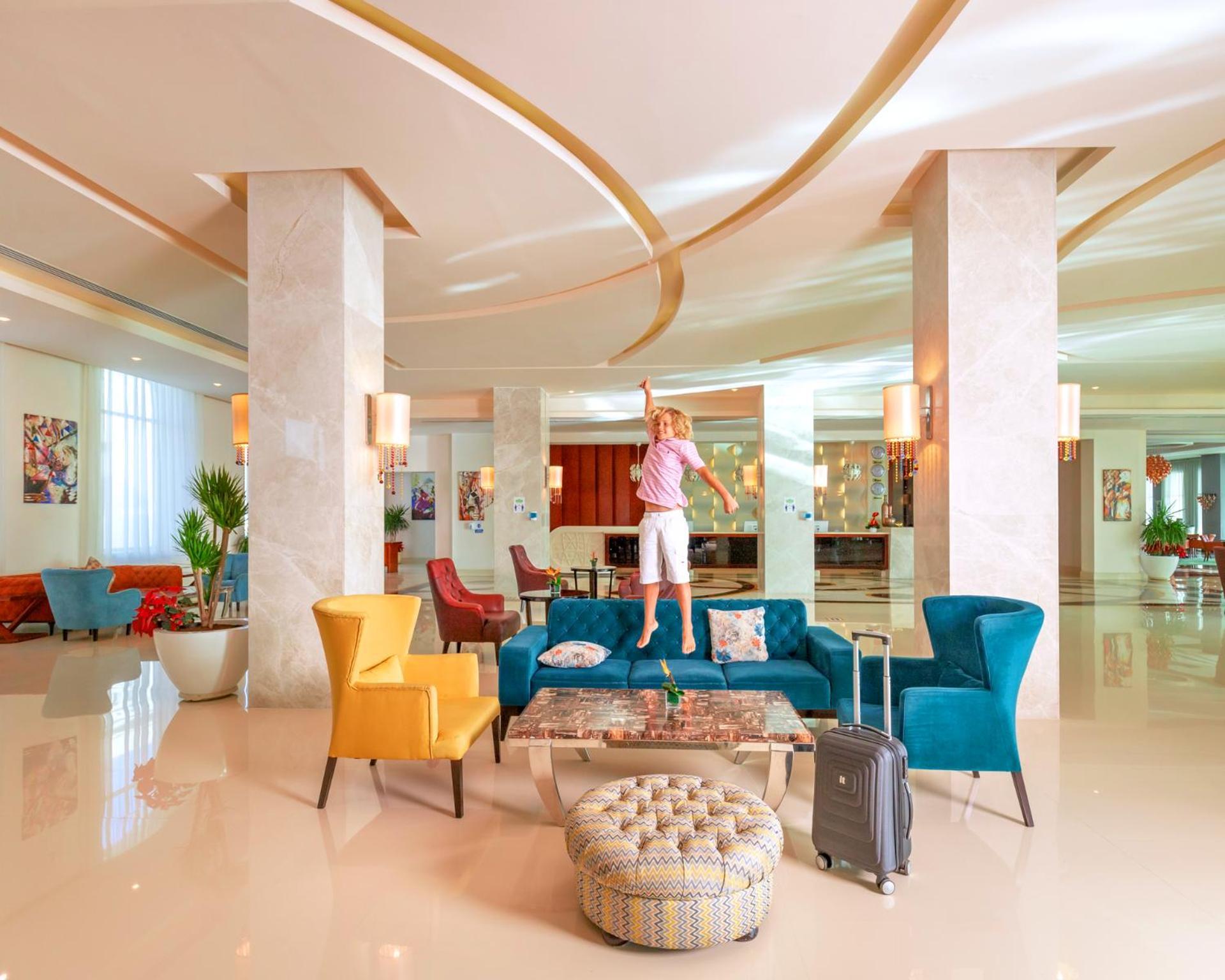 Hotel Royal Albatros Moderna - Families and couples only à Charm el-Cheikh Extérieur photo The photo shows a modern and stylish hotel lobby. There's a spacious area with elegant decor, featuring large pillars and contemporary lighting. A colorful arrangement of furniture includes teal, yellow, and red chairs. A person is standing on a larg