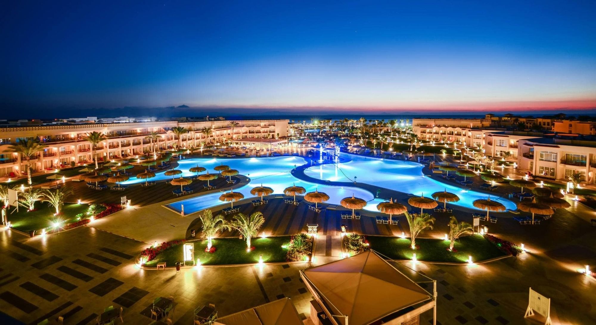 Hotel Royal Albatros Moderna - Families and couples only à Charm el-Cheikh Extérieur photo The photo showcases an elegant resort area at dusk. It features a large swimming pool, which is beautifully illuminated with blue lights, creating a serene and inviting atmosphere. Surrounding the pool are palm trees and umbrellas, enhancing the trop
